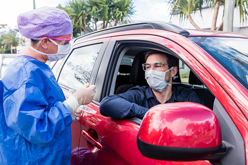 A doctor taking a nasal swab from a driver guy in car with mask taking test